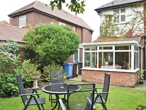 A patio with a round table and four chairs, surrounded by a garden with various plants and a large bush. - 3 bedroom accommodation in Fairhaven, near St Anne&rsquo;s (Fairhaven, near St Anne&rsquo;s)