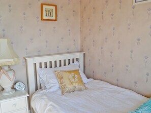 A bedroom with a white bed, a nightstand with a lamp, a framed picture on the wall, and a patterned wallpaper. - 3 bedroom accommodation in Fairhaven, near St Anne&rsquo;s (Fairhaven, near St Anne&rsquo;s)