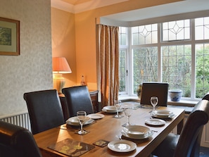 Une salle à manger avec une table en bois dressée pour six personnes, entourée de chaises, et une fenêtre donnant sur un paysage verdoyant.