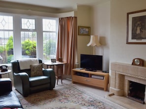 A living room with a sofa, TV, fireplace, and a view of greenery outside. - 3 bedroom accommodation in Fairhaven, near St Anne&rsquo;s (Fairhaven, near St Anne&rsquo;s)