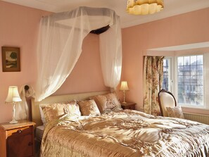 A bedroom with a canopy bed, bedside lamps, a framed picture on the wall, and a window with curtains.