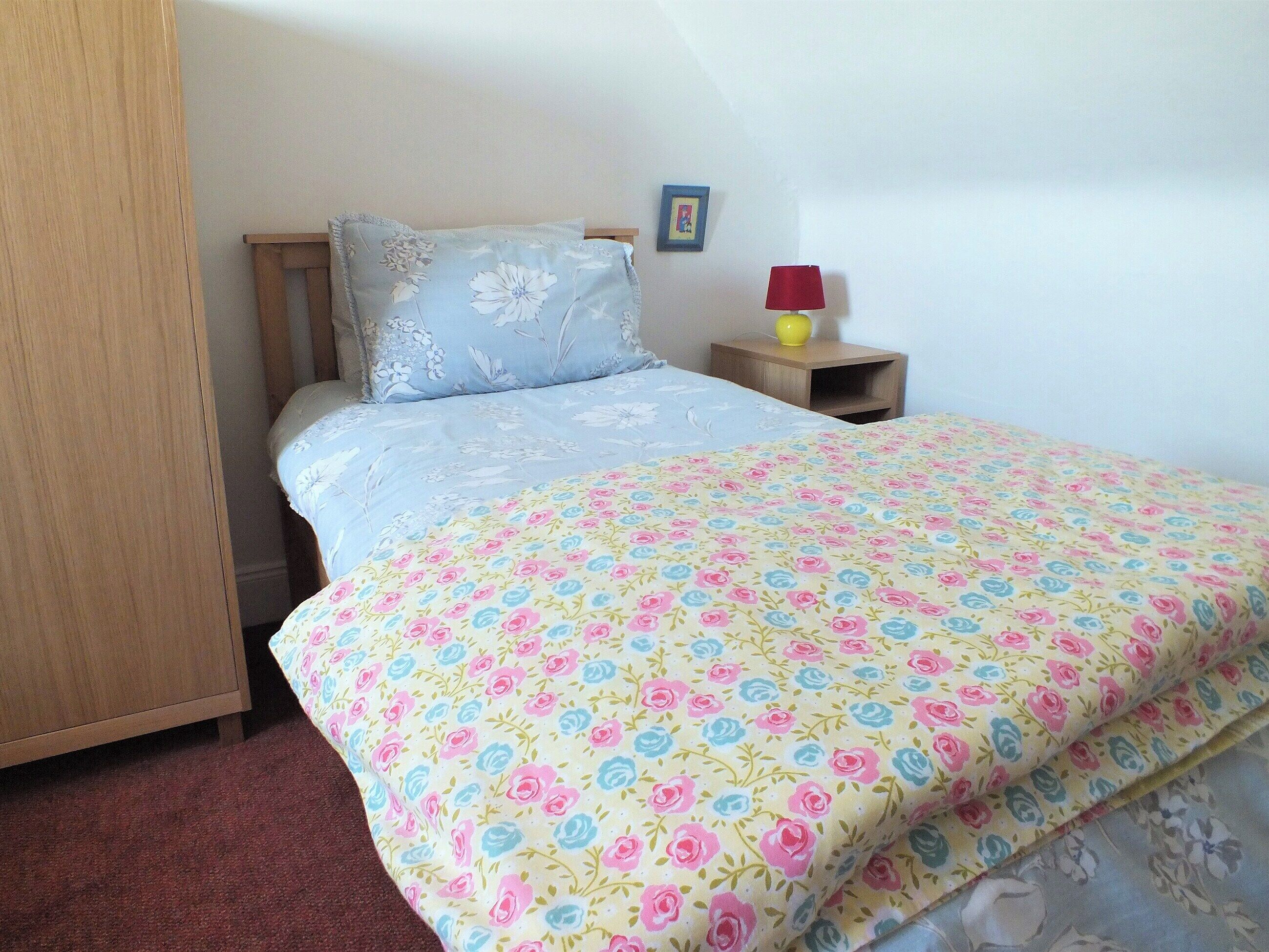 Ein Schlafzimmer mit Bett, Nachttisch, Lampe und einem Bildrahmen an der Wand.