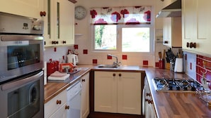 A kitchen with white cabinets, a built-in oven, a sink, and a window with floral curtains.