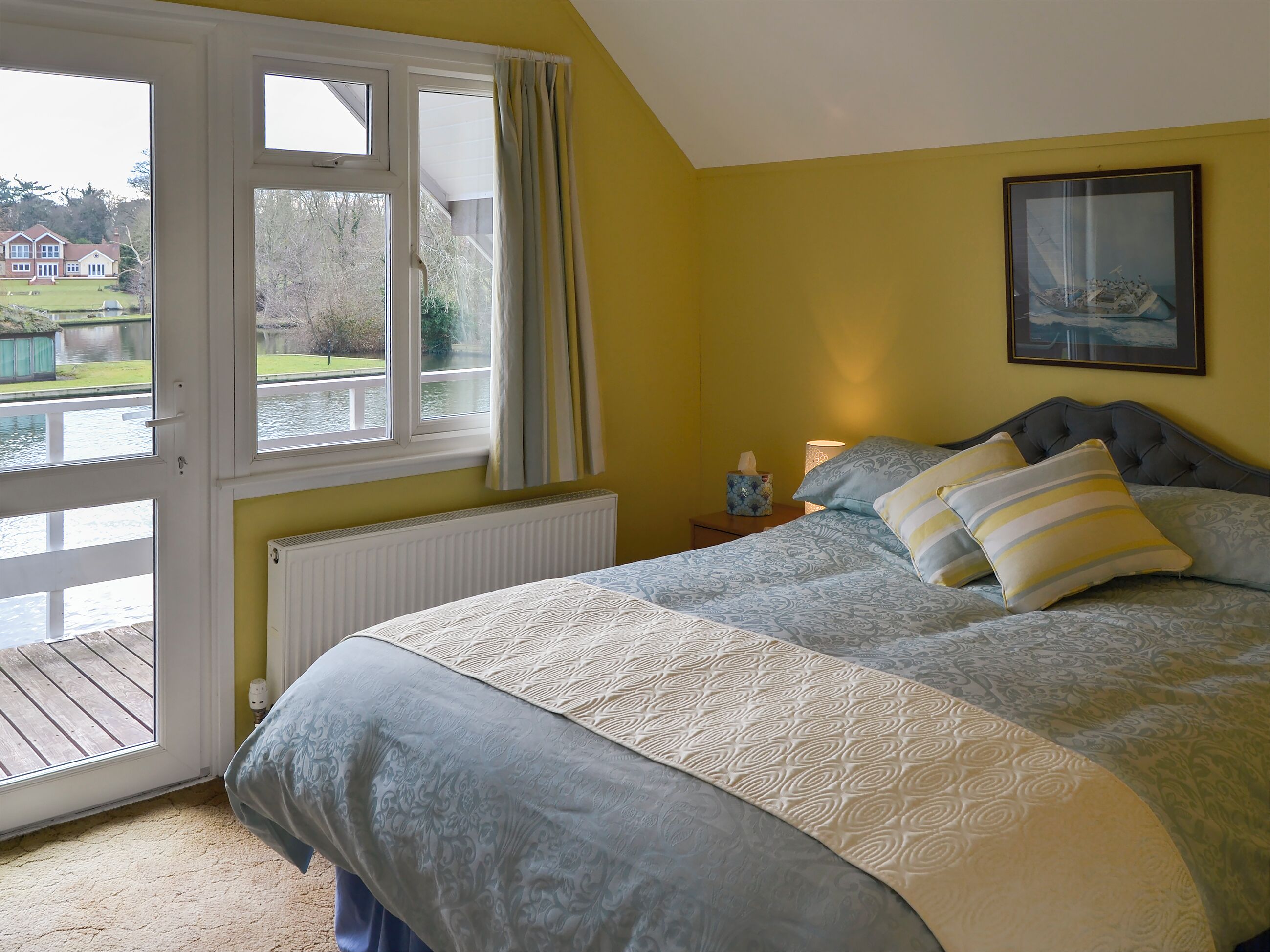 A bedroom with a bed, a window, a radiator, and a painting on the wall.