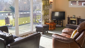 A living room with a TV, leather sofas, a wooden coffee table, and a sliding glass door leading to a deck.