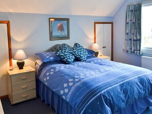 A bedroom with a bed, two bedside tables, a nightstand, a dresser, a framed picture on the wall, and a window with curtains.