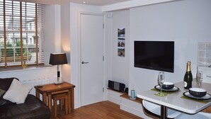 Uma sala de estar moderna com sofá, mesa de centro, televisão e área de jantar com mesa e cadeiras.