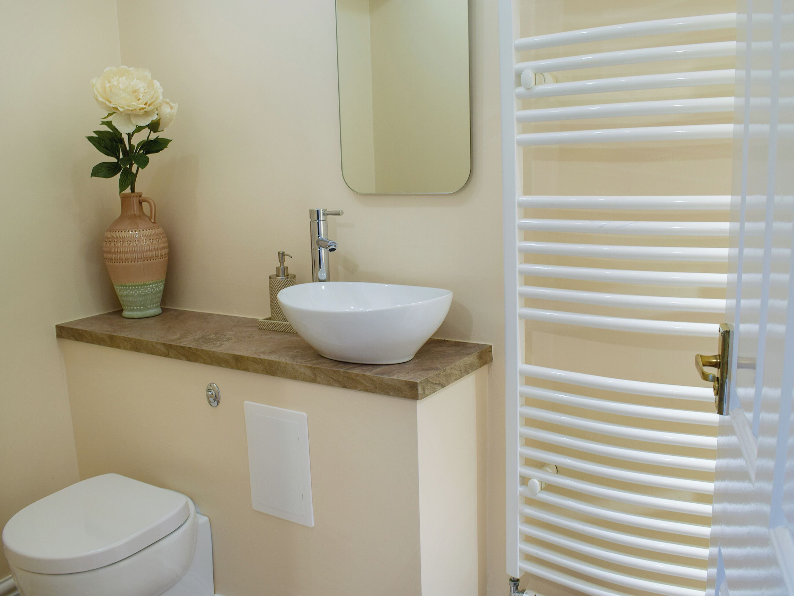 Une salle de bain avec un lavabo blanc, un vase de fleurs, des toilettes et un miroir au mur.