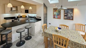 Een moderne keuken met een centraal eiland, barkrukken en een eettafel met stoelen.