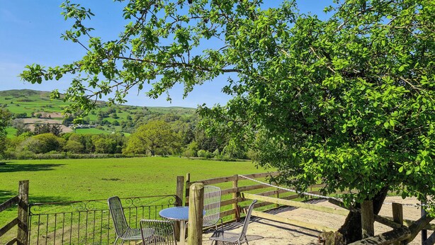 A rustic outdoor seating area with metal chairs and a table, surrounded by a wooden fence and a tree. - 3 bedroom accommodation in Bala (Bala)