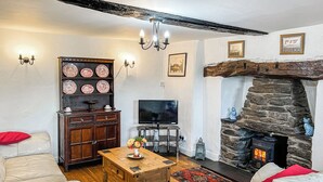 A cozy living room with a stone fireplace, white leather sofas, a wooden coffee table, and a television. - 3 bedroom accommodation in Bala (Bala)