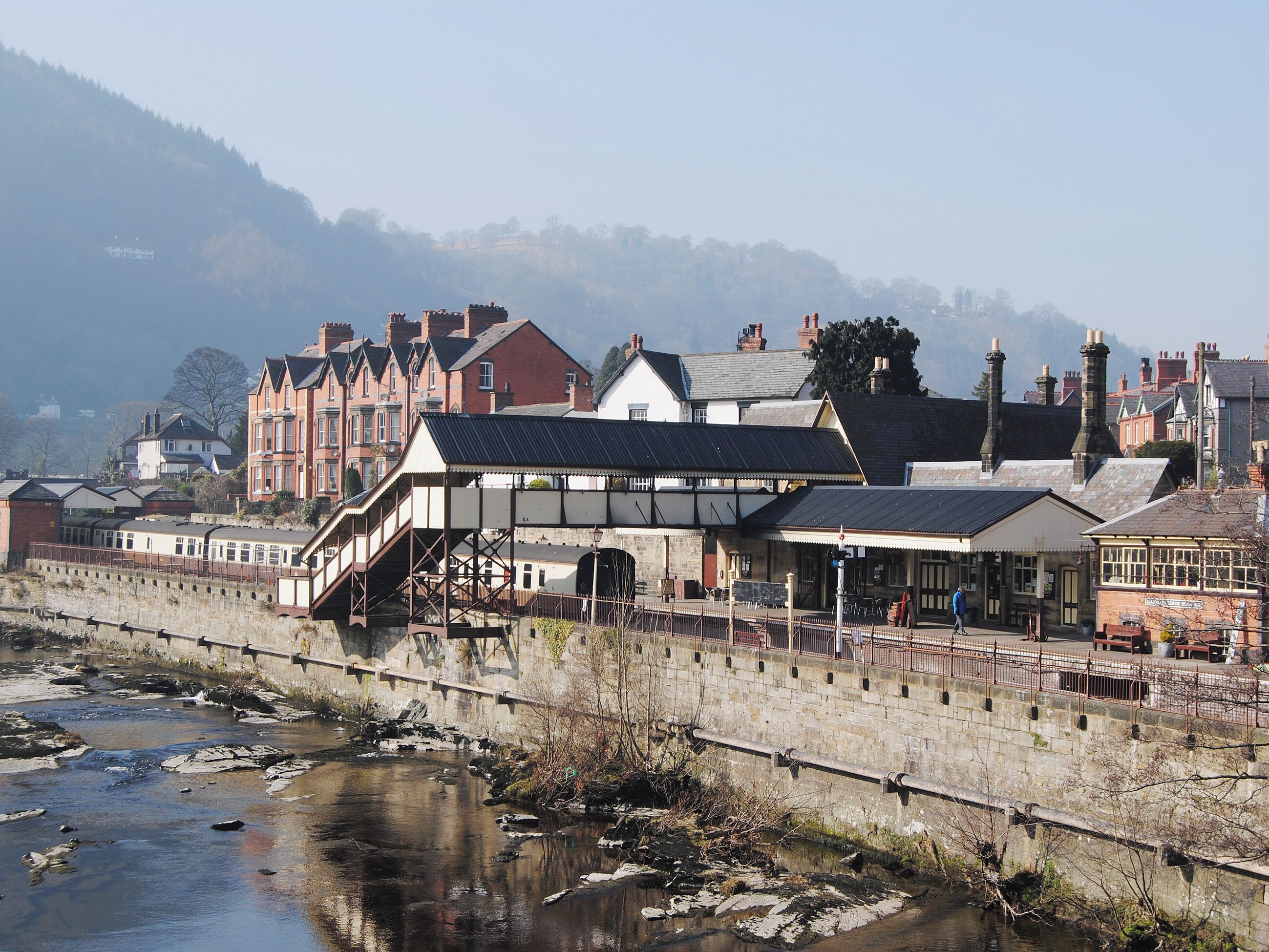 A riverside building with a bridge, stone walls, and a train.