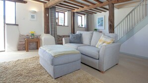 A cozy living room with a grey sofa, a matching ottoman, and a wooden ceiling.