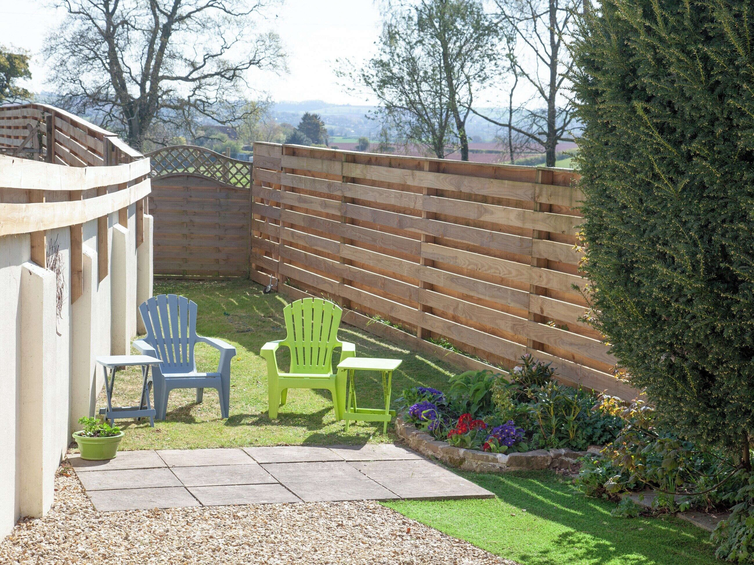 A patio area with two Adirondack chairs, a small table, and a wooden fence.