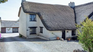 A traditional thatched-roof house with a gravel driveway and potted plants.