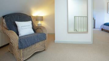 A wicker chair with a cushion labeled "retreat" and a lamp in a room with a large mirror and a bed in the background.