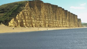 Eine Küstenklippe mit einem Strand im Vordergrund.