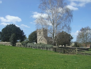 A stone building with a tower, surrounded by a stone wall and a wooden fence, set in a grassy field with trees. - 2 bedroom accommodation in Bothenhampton, near Bridport (Bothenhampton, near Bridport)