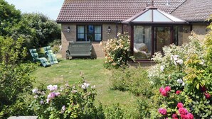 A house with a tiled roof, a glass door entrance, and a garden with various plants and flowers. - 3 bedroom accommodation in Walcott (Walcott)