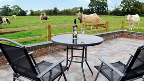 Une terrasse extérieure avec une table ronde et deux chaises, une clôture en bois et des vaches en arrière-plan.