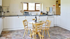 Une cuisine avec des meubles blancs, une table à manger avec quatre chaises et une fenêtre au-dessus de l’évier.