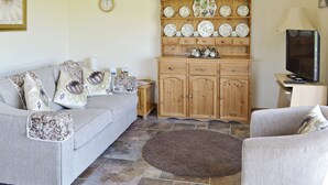 Un salon avec un canapé gris, un meuble en bois orné d’assiettes décoratives, un téléviseur et une table basse.