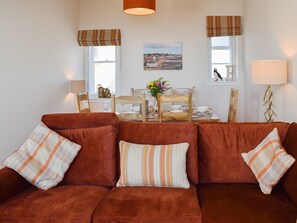 A living room with a brown sofa, plaid cushions, a dining table set with glassware, and a painting on the wall. - Harbourside Apartment (Anstruther)