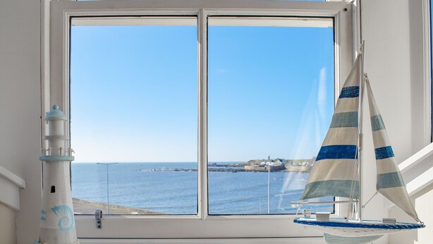 A window with a view of the sea, a lighthouse model, and a sailboat model. - Harbourside Apartment (Anstruther)