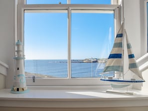 A window with a view of the sea, a lighthouse model, and a sailboat model. - Harbourside Apartment (Anstruther)