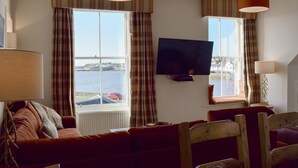 A living room with a television, two windows with curtains, a sofa, and a chair. - Harbourside Apartment (Anstruther)