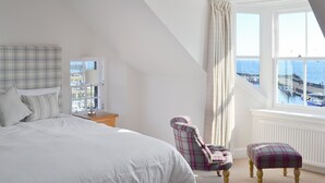 A bedroom with a bed, a chair, a window with a view of the sea, and a lamp. - Harbourside Apartment (Anstruther)