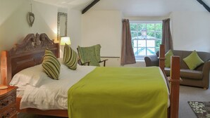 Un dormitorio con cama de madera, una colcha verde, una silla de madera, un sofá, una ventana con cortinas y una lámpara.