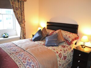 Cozy retreat with a neatly made bed, nightstand, and dresser, offering a peaceful view.