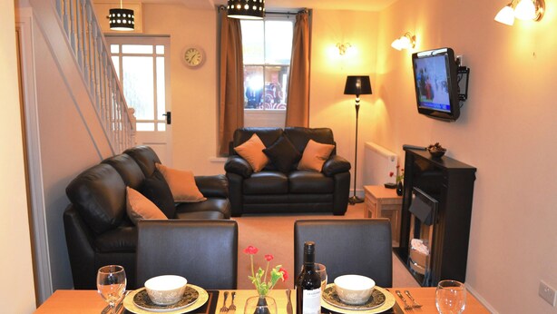 Un coin repas avec une table dressée pour deux personnes, une cheminée et un téléviseur fixé au mur.