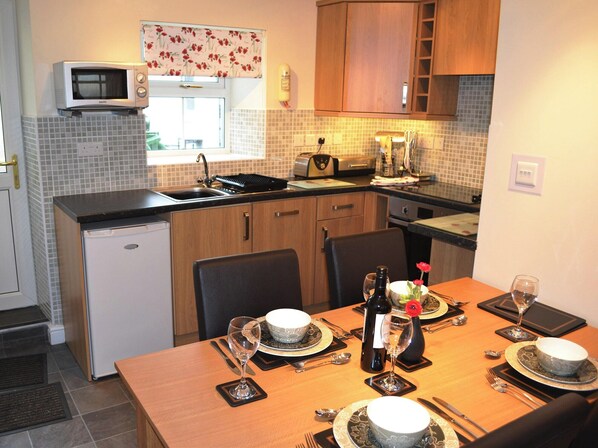 Compact kitchen with a microwave, toaster, sink, dining area, and table for two.