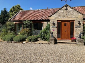 A stone building with a tiled roof, a wooden door, and a small garden area with pebbles and shrubs. - All on the Ground Floor: 
Open plan living space. (Lockton, near Pickering)