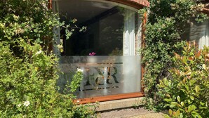 Une maison dotée d’une grande fenêtre, entourée de verdure et bordée d’un chemin en pierre.