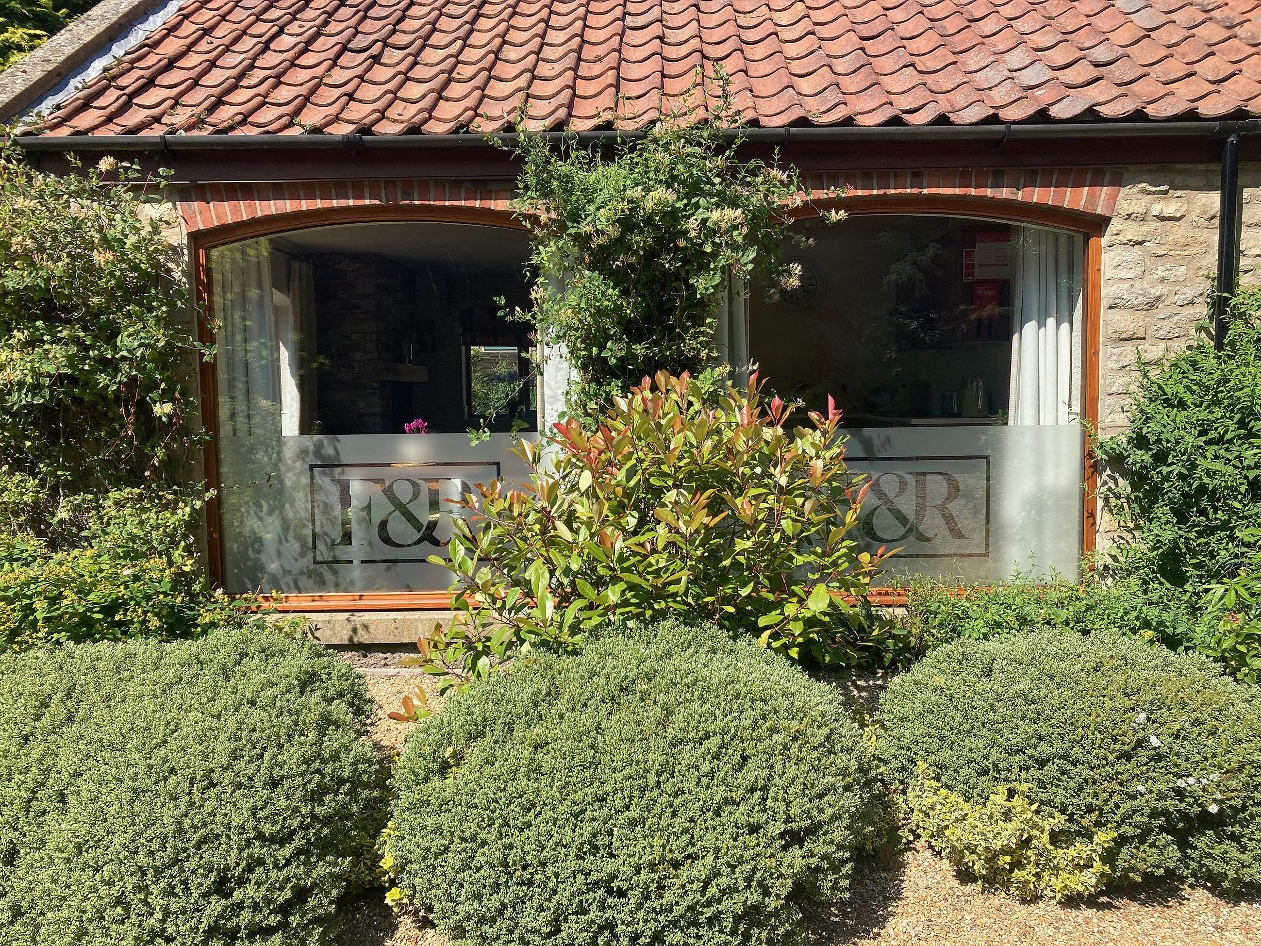 A building with a tiled roof, a large window with a metal frame, and a sign with "&R" visible.