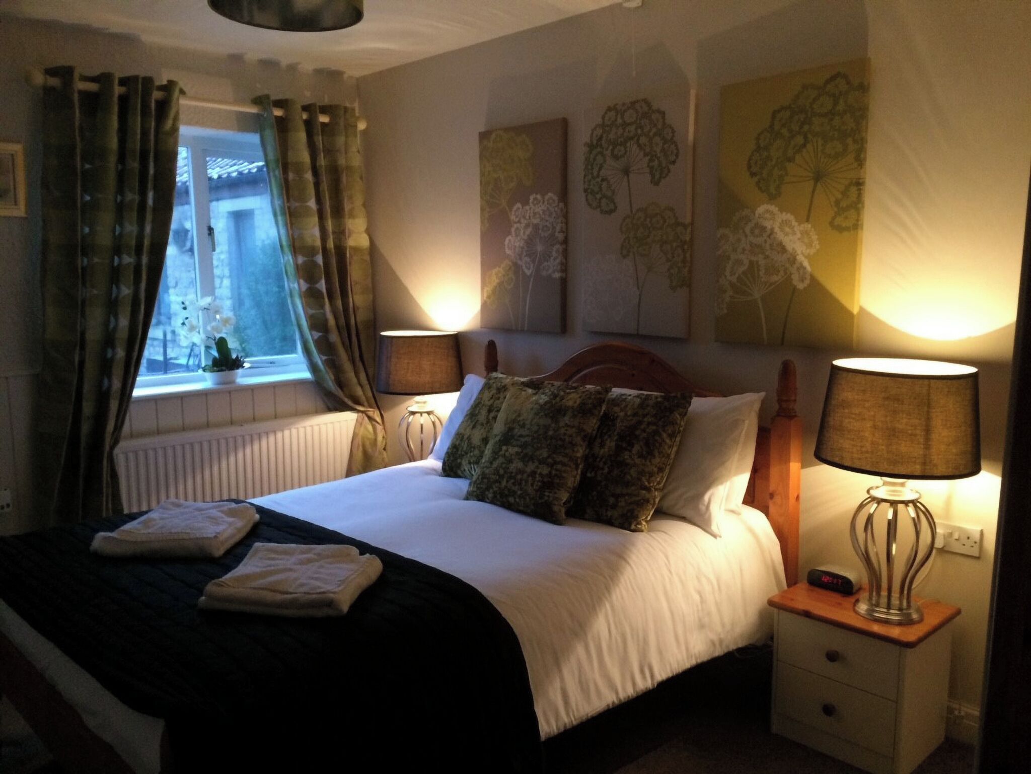 A neatly made bed with a black and white duvet, two pillows, and folded towels on a wooden nightstand. There are two wall-mounted lamps on either side of the bed.