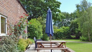 A patio with a wooden table and chairs, a blue umbrella, and a brick wall. - 1 bedroom accommodation in Ulrome near Bridlington (Ulrome near Bridlington)