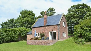 A brick house with a sloped roof, a chimney, and a small patio with a table and chairs. - 1 bedroom accommodation in Ulrome near Bridlington (Ulrome near Bridlington)