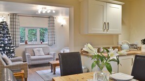 A cozy living room with a fireplace, a dining table set for two, and a kitchen area with cabinets and a toaster. - 1 bedroom accommodation in Ulrome near Bridlington (Ulrome near Bridlington)