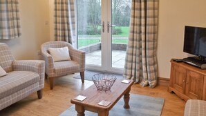 A living room with a sofa, armchair, and a television on a wooden cabinet. - 1 bedroom accommodation in Ulrome near Bridlington (Ulrome near Bridlington)