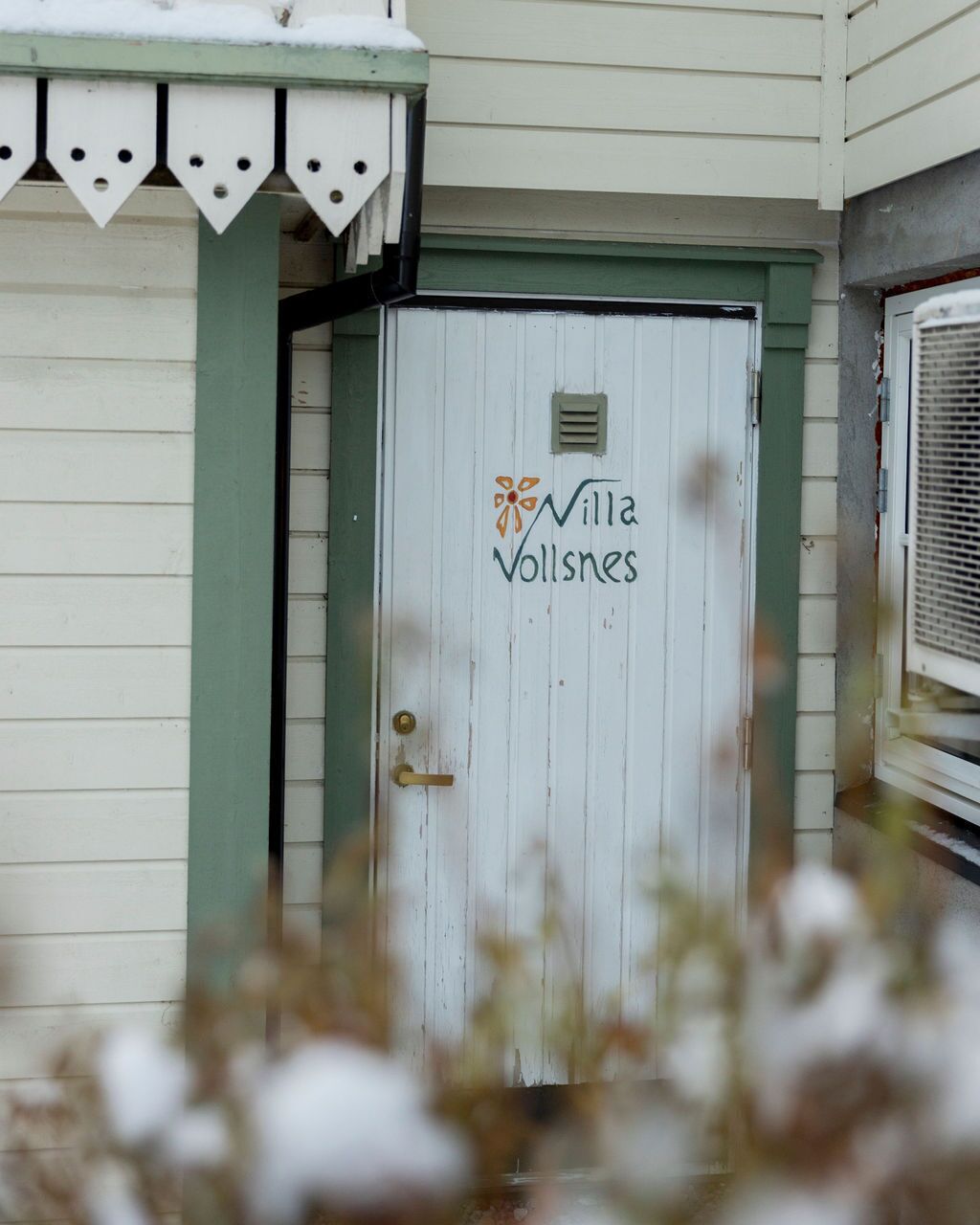 A white door with the text "Villa Vollsnes" and a logo, surrounded by a green frame.