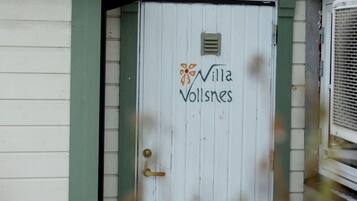 A white door with the text "Villa Vollsnes" and a logo, surrounded by a green frame.