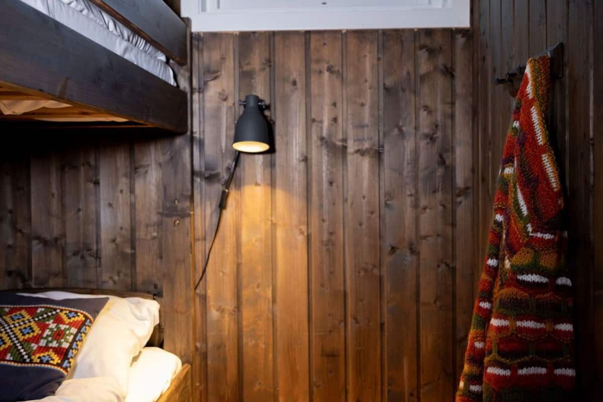 Una habitación tipo cabaña acogedora con una litera, una ventana pequeña, una lámpara y una manta colorida.