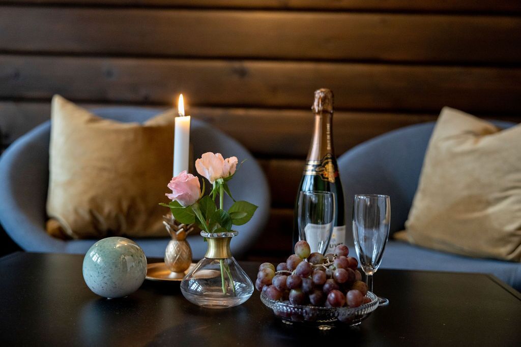 A table with a candle, a vase with flowers, a bottle of champagne, a bowl of grapes, and a glass.