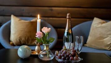 A table with a candle, a vase with flowers, a bottle of champagne, a bowl of grapes, and a glass.