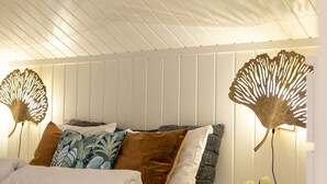 A bedroom with a bed, pillows, a bedside table, and a wall-mounted lamp.