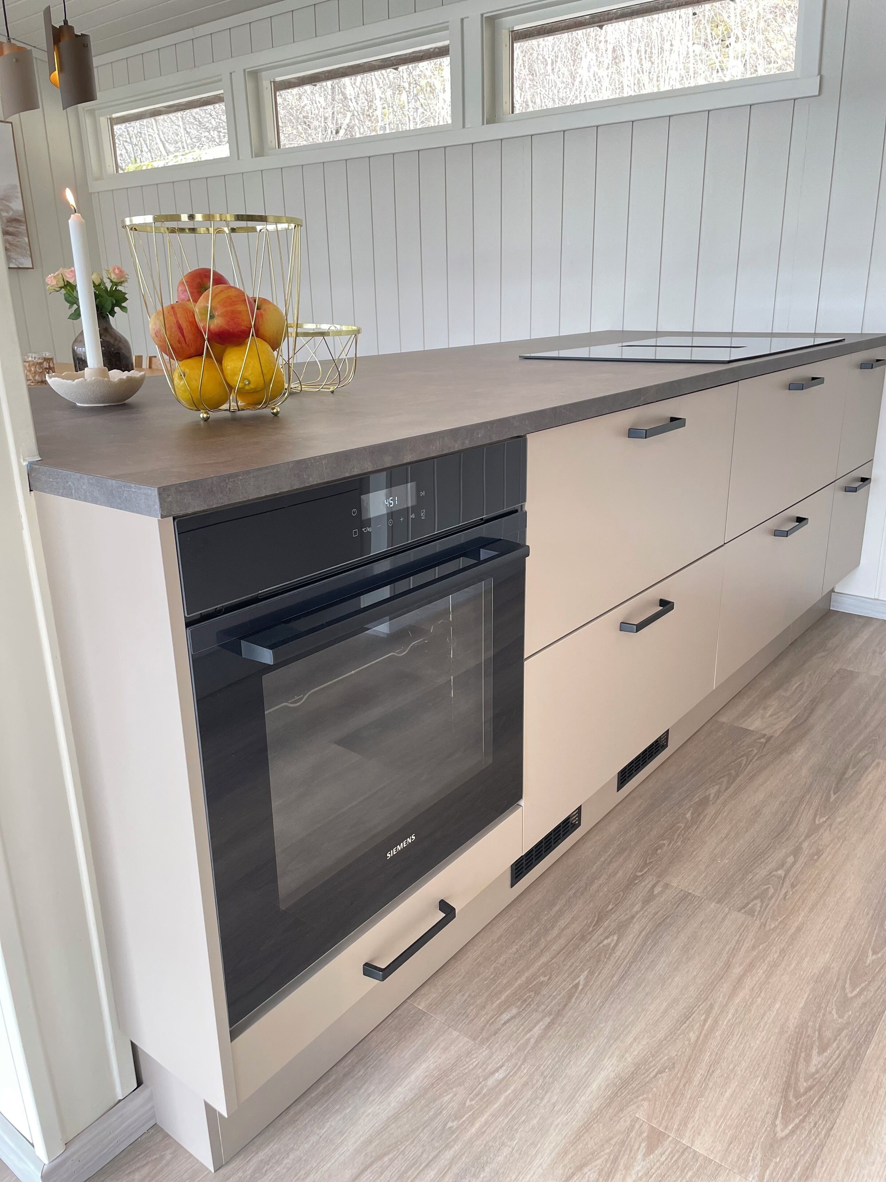 A modern kitchen with a built-in oven, a fruit basket, and a window above the countertop.
